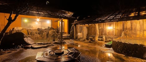 Un onsen japonés tradicional con un baño de madera, entorno de piedra y una cálida iluminación interior.