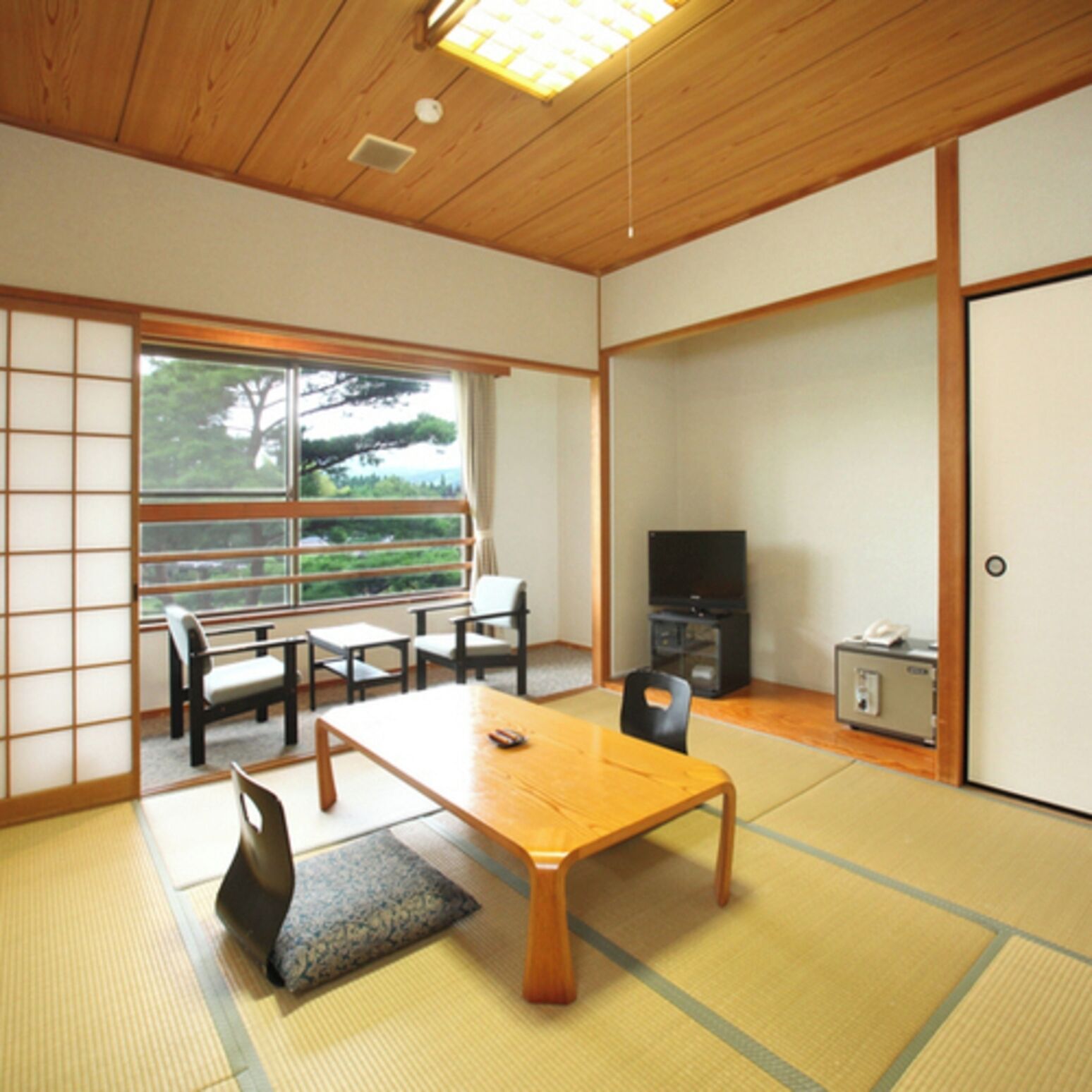 A traditional Japanese room with tatami flooring, a low table, chairs, a television, and a sliding door.