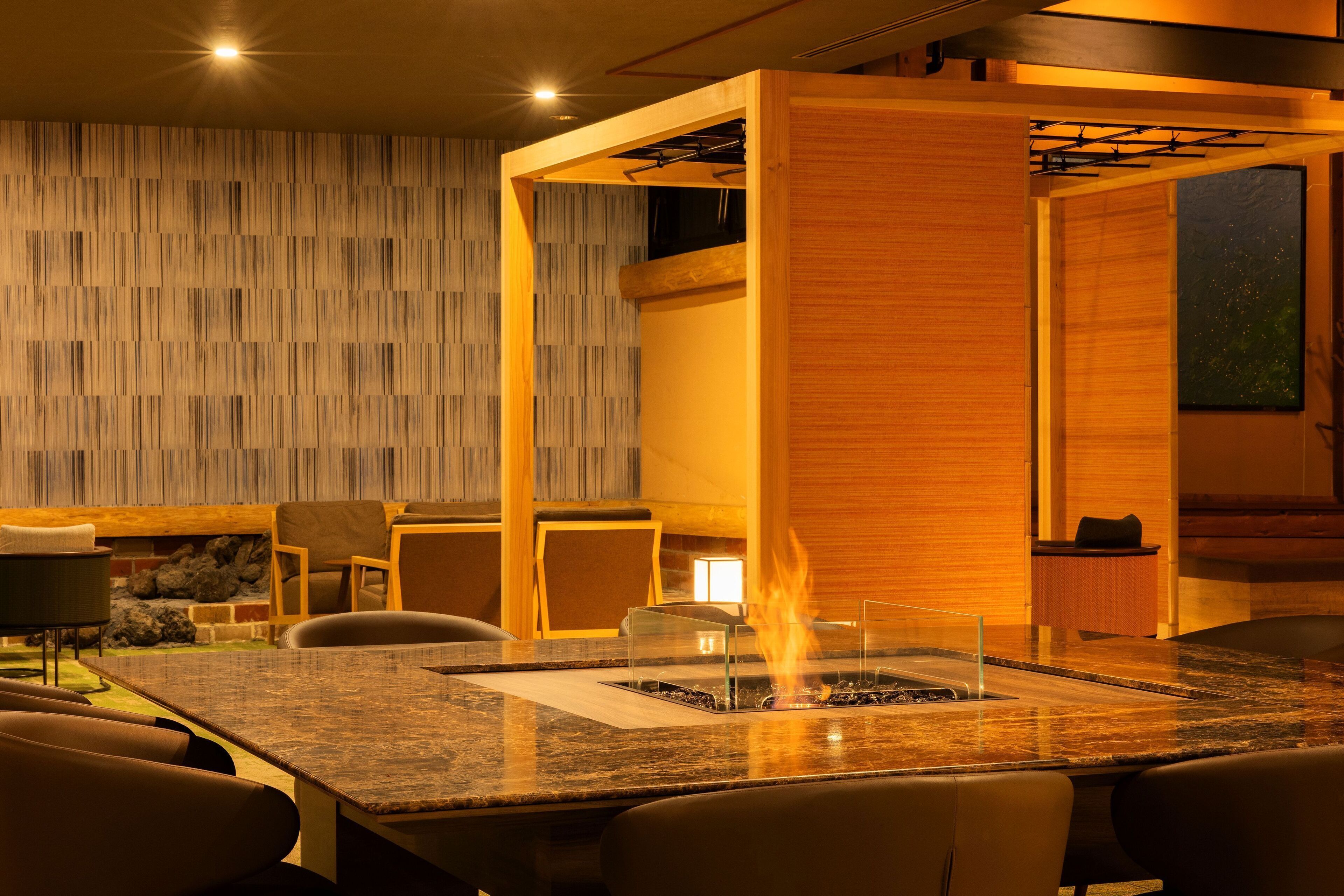 Un comedor moderno con una chimenea central, paneles de madera y mobiliario contemporáneo.