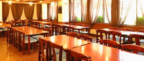 A large dining hall with multiple wooden tables and chairs, arranged in rows.