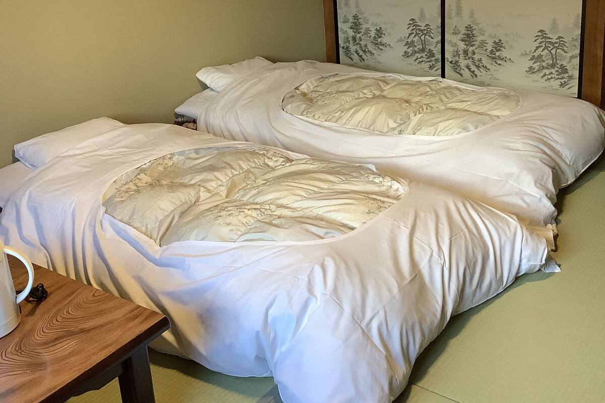 A traditional Japanese room with tatami flooring, a low wooden table, and a bed with white bedding.