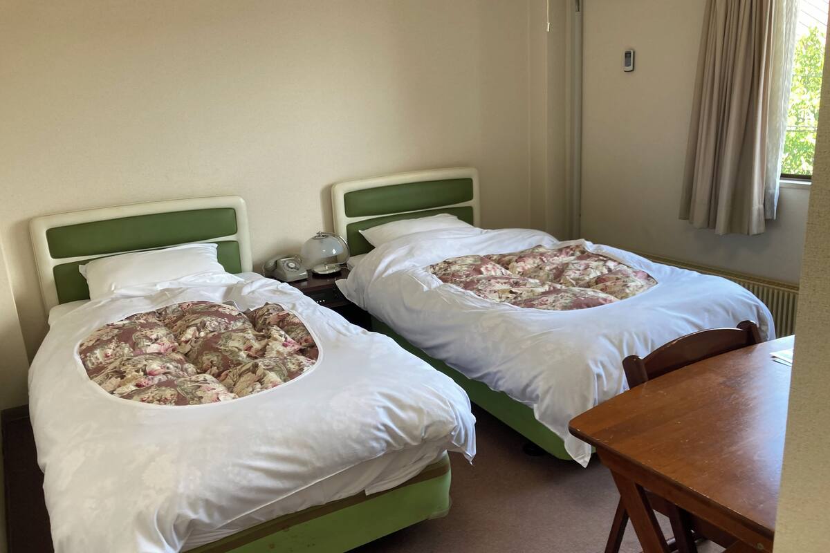 A twin room with two single beds, a wooden table, and a nightstand with a lamp.