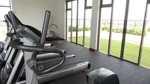 Ein Fitnessraum mit Laufbändern und einem Ergometer, großen Fenstern und Blick auf eine grüne Außenanlage.