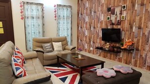 Una sala de estar con sofá, reposapiés, mesa de centro y televisión en una pared de madera.