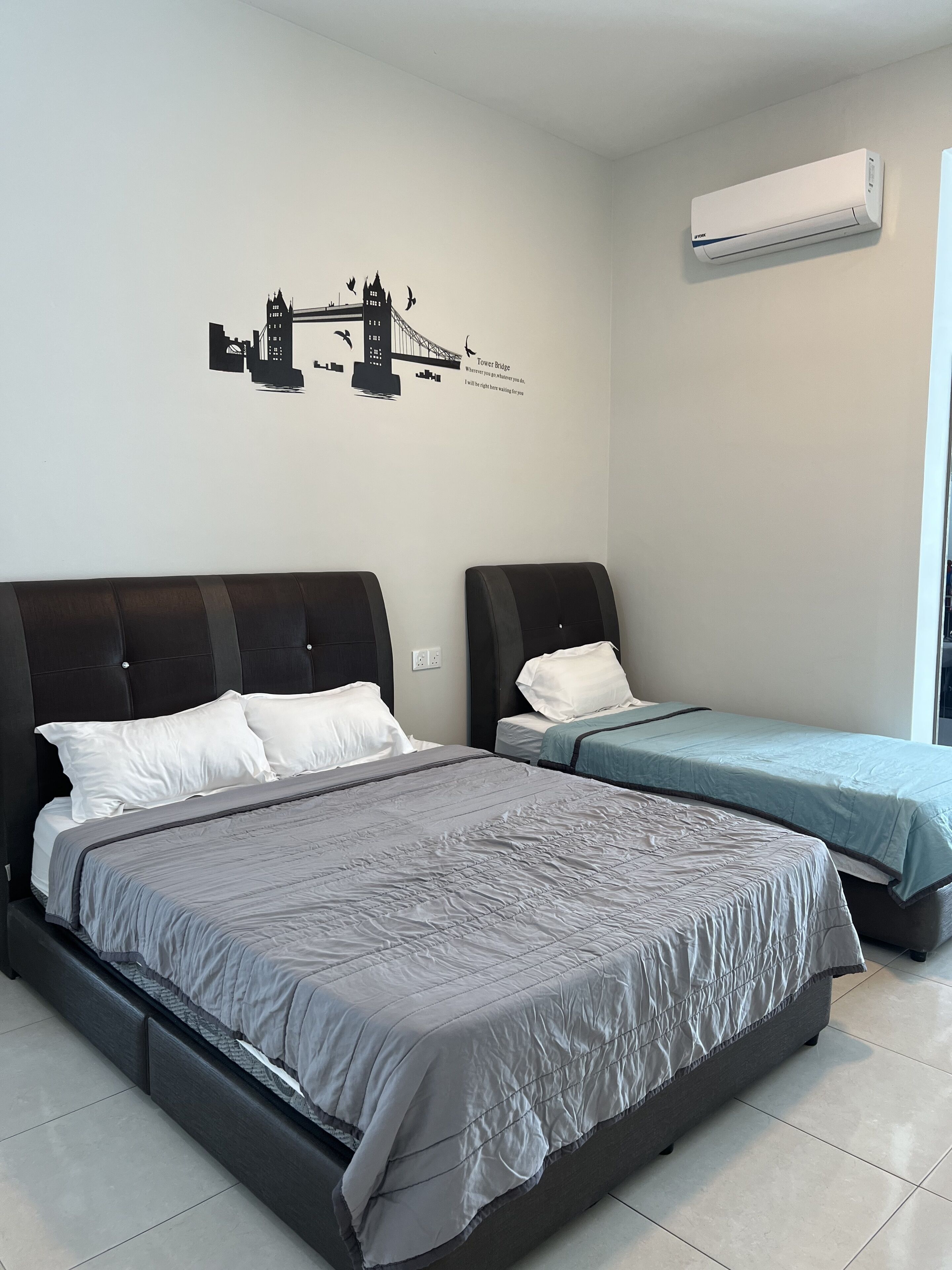 A hotel room with two beds, a wall mural of a bridge, and an air conditioning unit.