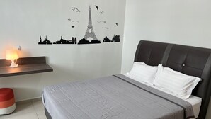Una cama bien hecha con colcha gris y almohadas blancas, una mesita de noche con lámpara y un adhesivo mural con monumentos parisinos.