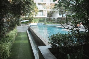 A swimming pool with steps leading into it, surrounded by greenery and a building in the background.