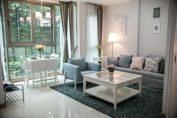 A modern living room with a white coffee table, grey sofa, and a dining table with chairs.