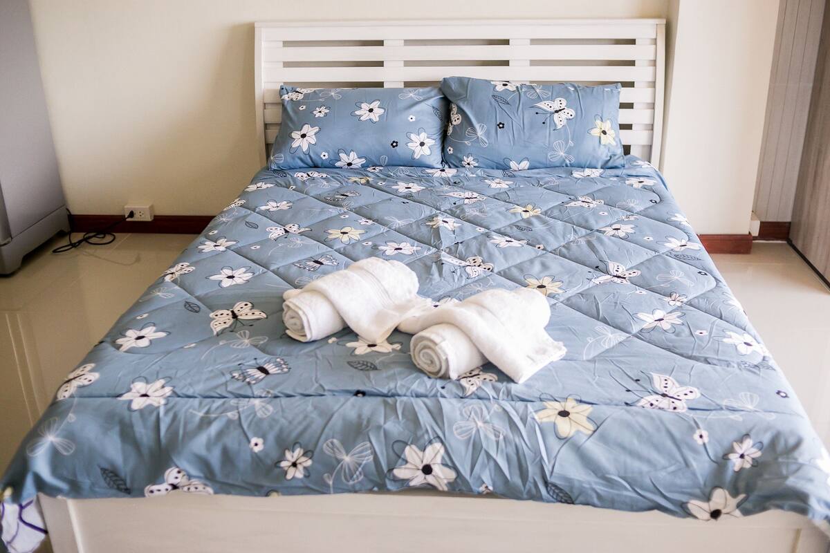 A neatly made bed with a floral blue quilt, white headboard, and two pillows.