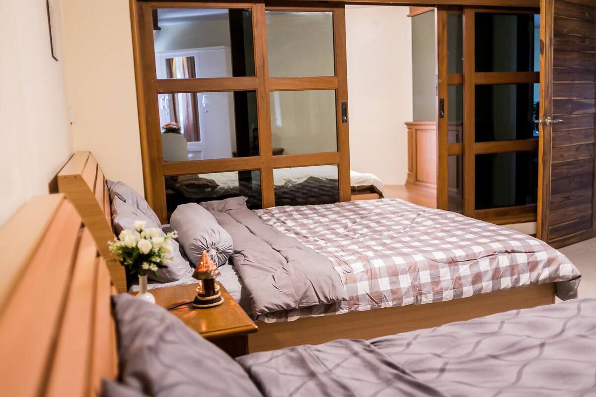 A bedroom with a large bed, a nightstand with a lamp, and a wooden wardrobe.