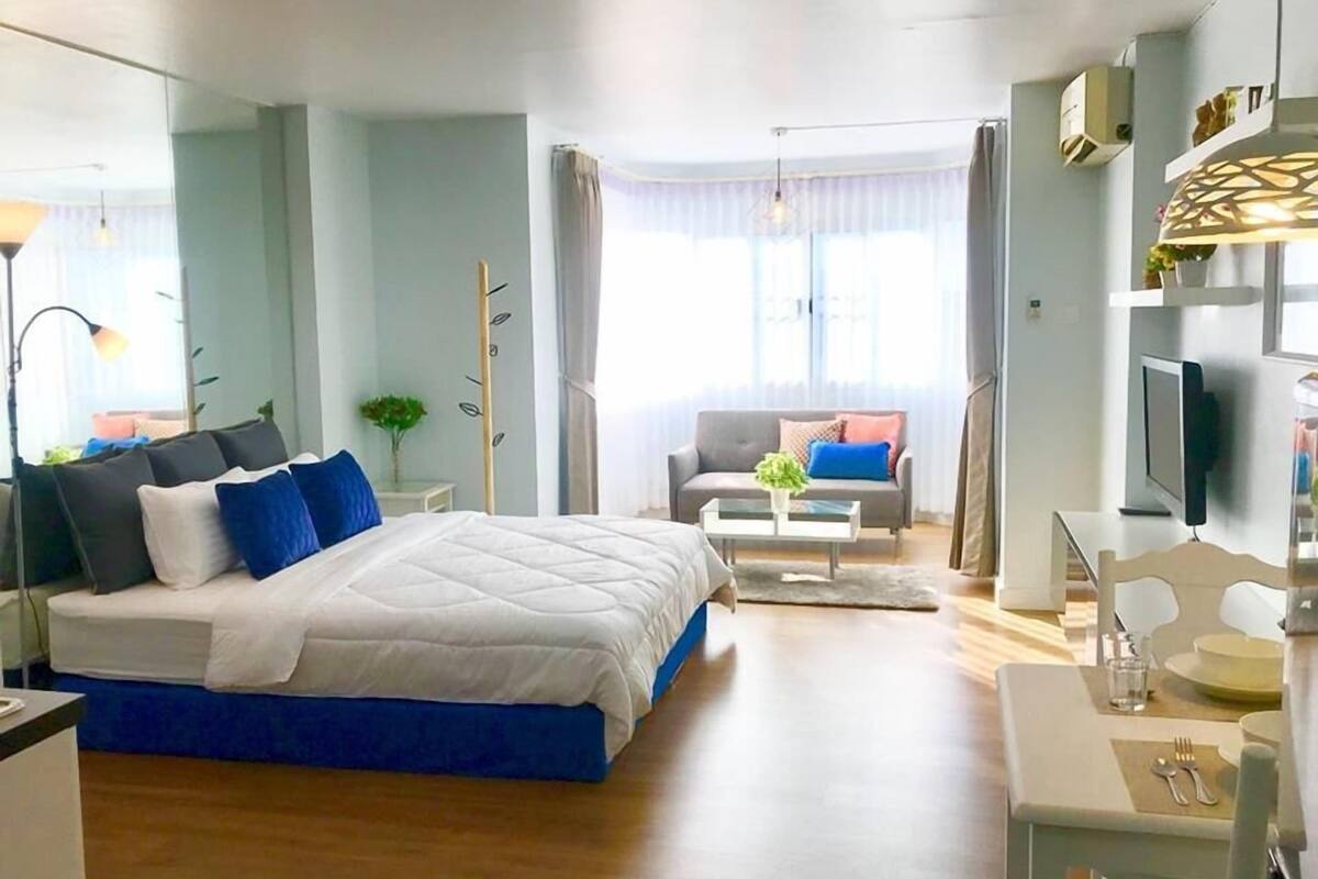 A modern hotel room with a large bed, a sofa, a dining table, and a TV.