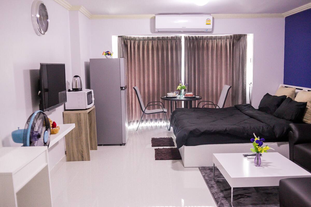 A modern hotel room with a bed, a desk, a chair, a TV, a refrigerator, and a window with curtains.