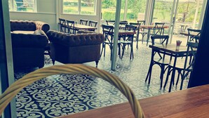 A dining area with a large window, a sofa, and a table with a basket of biscuits. - The Waterlily Gardens (Waihi)