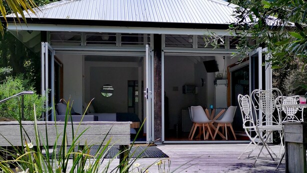 A modern house with a covered patio, outdoor seating, and a view of the surrounding greenery. - The Waterlily Gardens (Waihi)