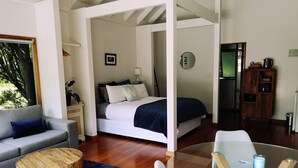 A modern room with a bed, a sofa, a coffee table, and a glass table with chairs. - The Waterlily Gardens (Waihi)