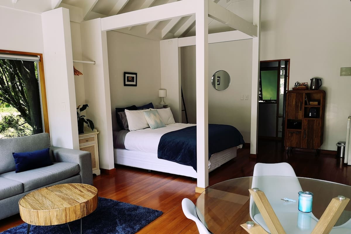 A modern room with a bed, a sofa, a coffee table, and a glass table with chairs.