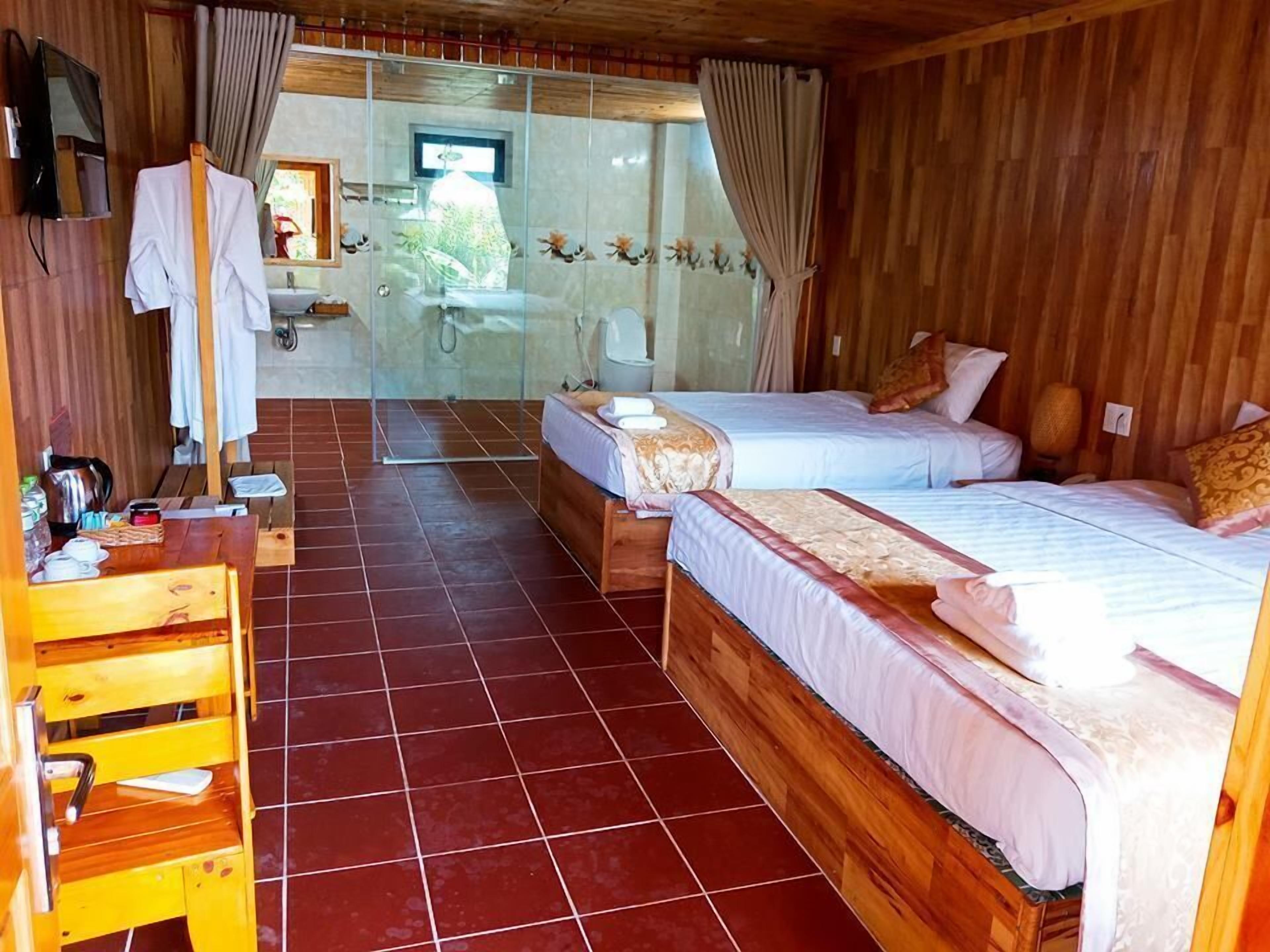 A room with two beds, a wooden desk, a television, and a shower area.