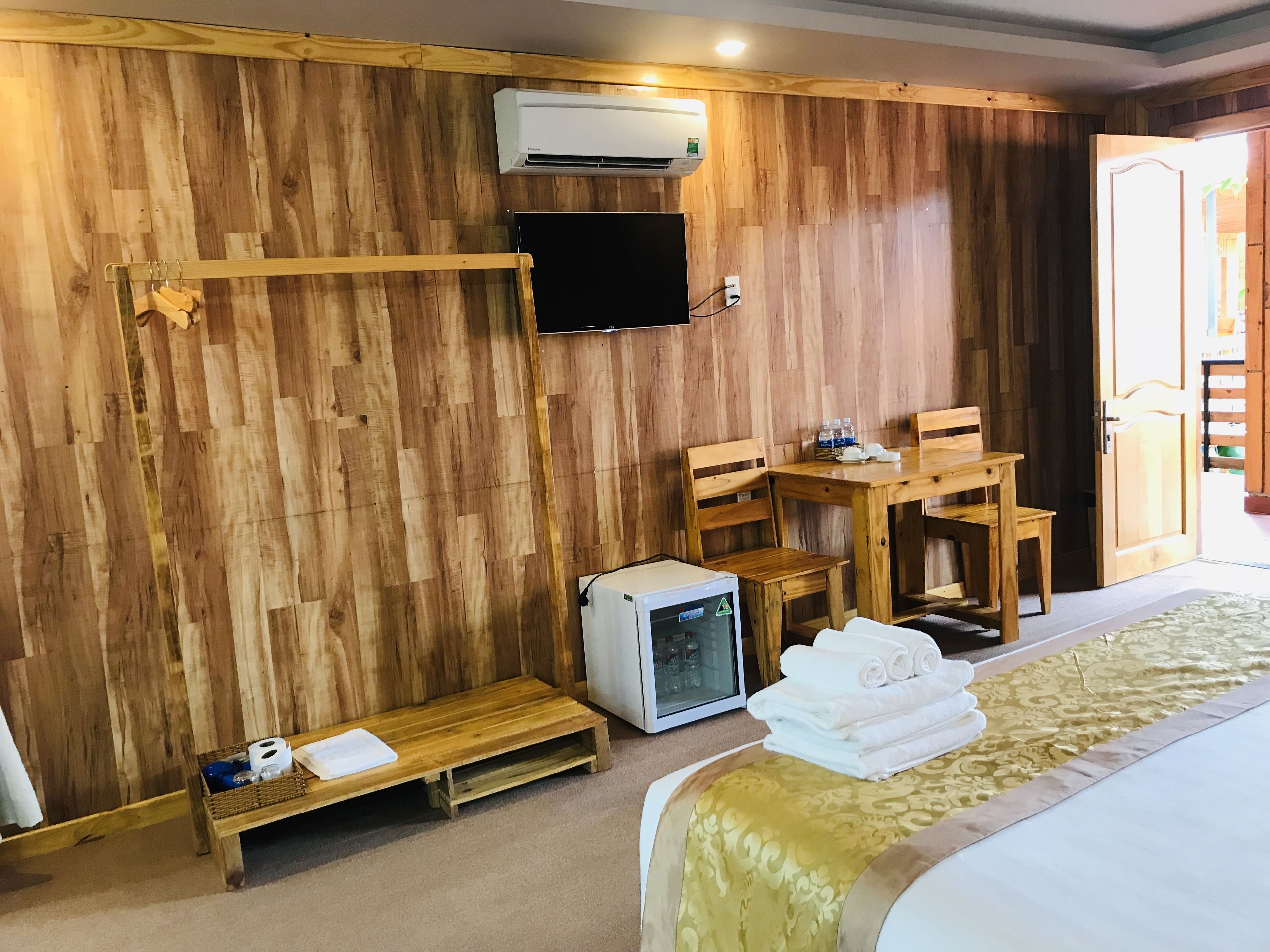 A wooden room with a bed, a small TV, a bench, and a table with chairs.