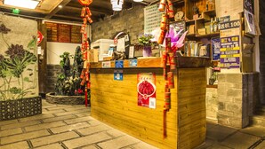 Un comptoir d’accueil avec un revêtement en bois, une machine à café et un vase rempli de fleurs. On y trouve également des panneaux avec du texte et un mur orné d’une fresque florale.