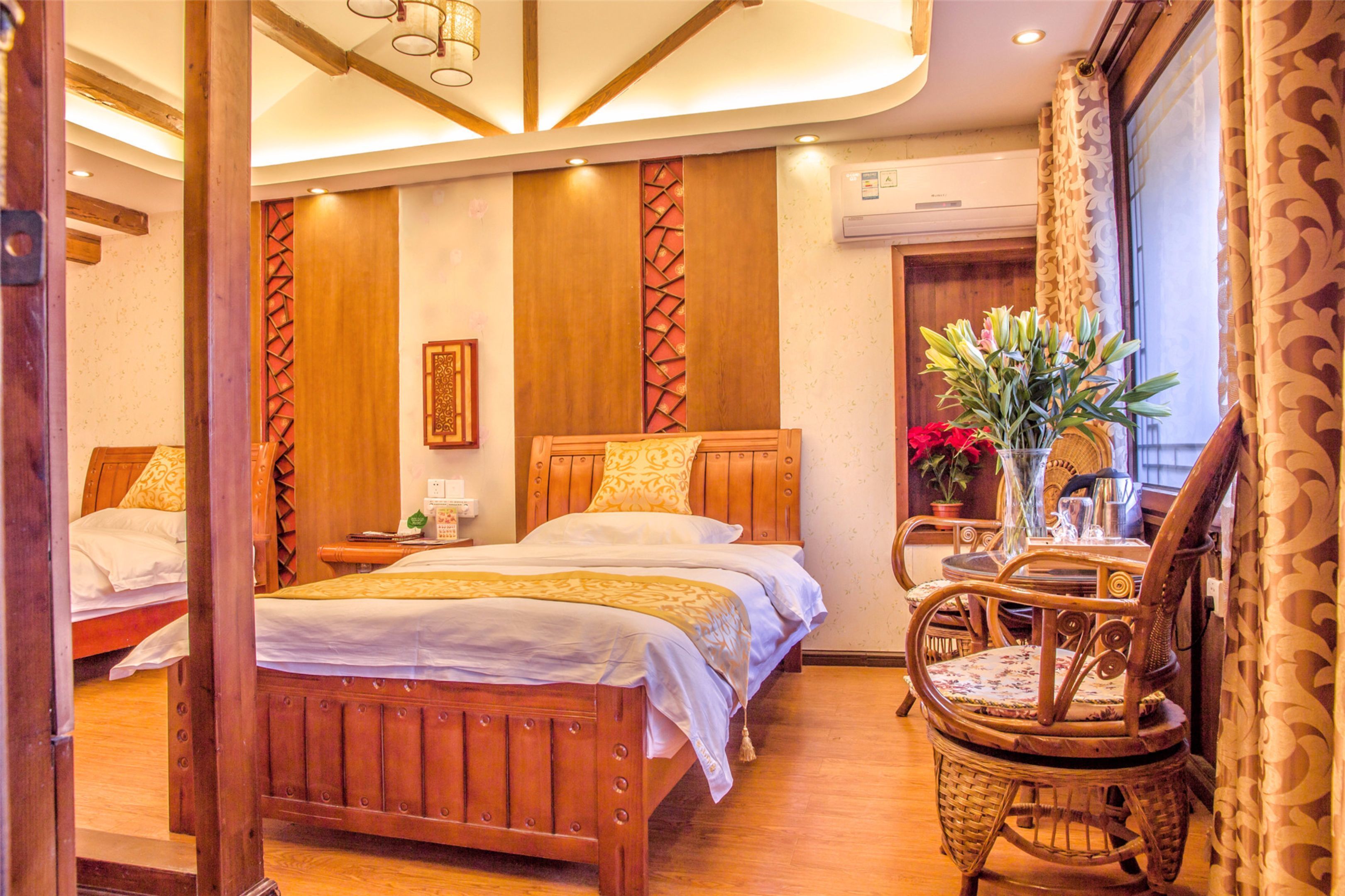 A hotel room with two wooden beds, a wooden chair, a table, and a vase with flowers.
