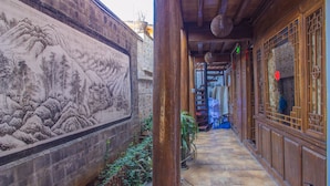 Un couloir étroit, avec une fresque sur le mur de gauche, des portes en bois sur le mur de droite et un sol carrelé.