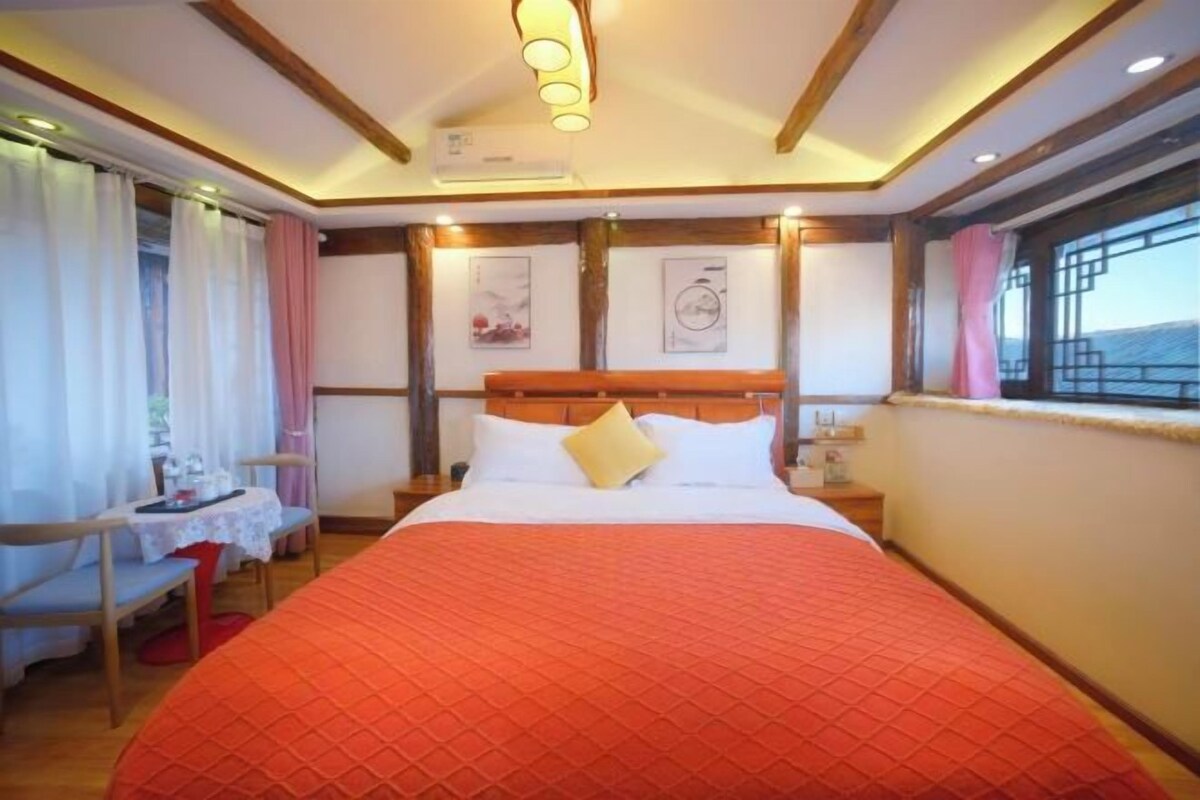 A hotel room with a large bed, bedside tables, a desk, and a window with curtains.