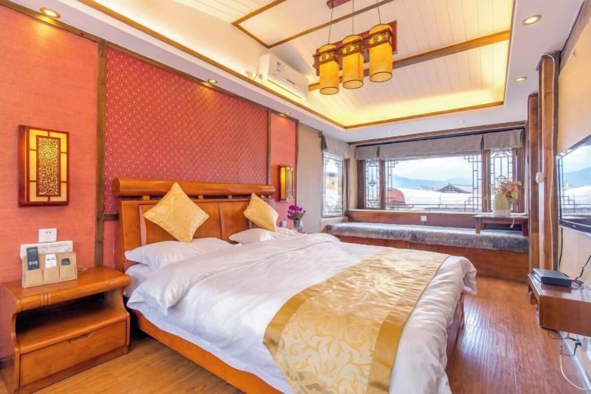 A hotel room with a large bed, wooden headboard, bedside tables, and a window with a view.
