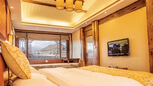 Une chambre d’hôtel avec un grand lit, un téléviseur fixé au mur et une vue sur les montagnes par la fenêtre.