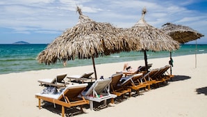 Una spiaggia con lettini di legno e ombrelloni di paglia.