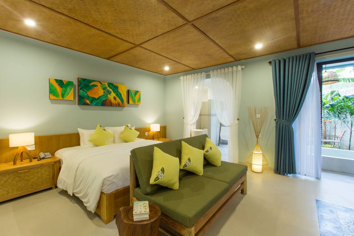 Una habitación de hotel con una cama, un sofá, una mesita de noche y una lámpara.