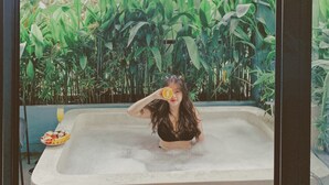 Una donna in vasca da bagno con un murale tropicale sullo sfondo.