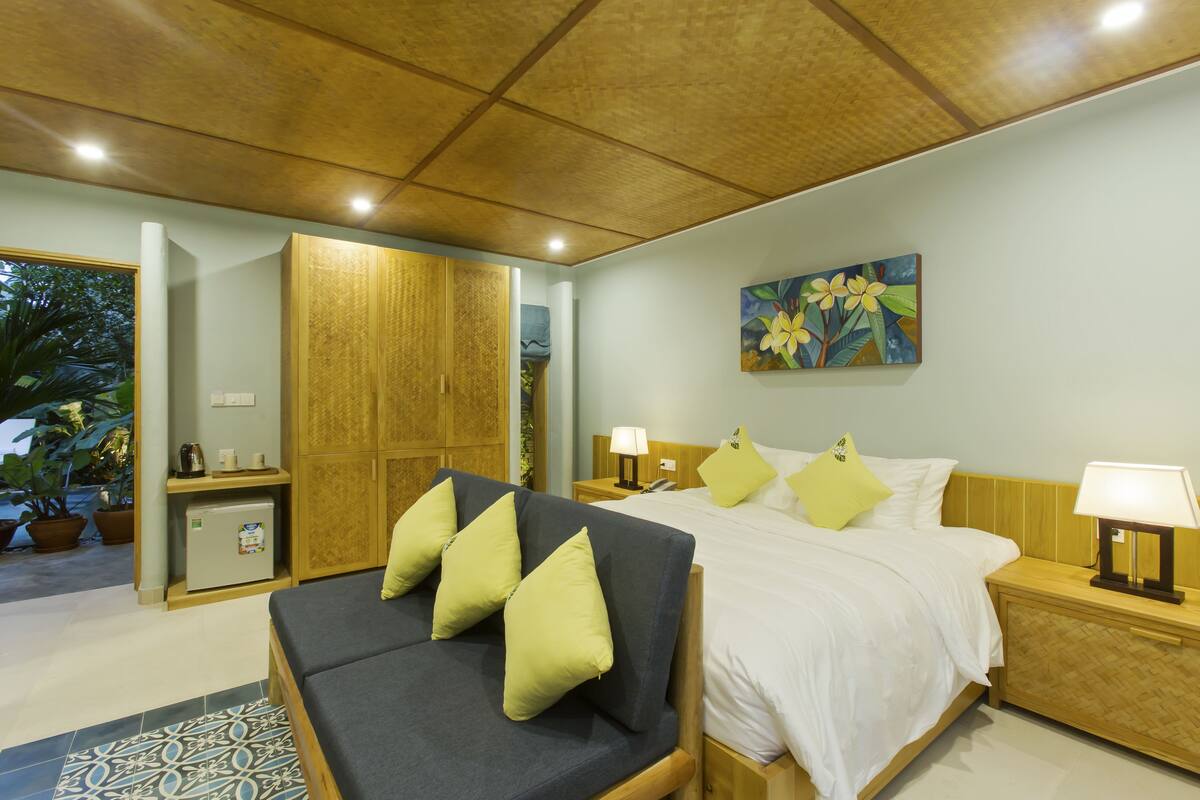 Un dormitorio con cama, mesitas de noche, un pequeño refrigerador y un cuadro en la pared. Incluye un sofá con cojines.