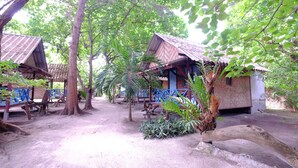 A rustic outdoor area with thatched-roof huts, surrounded by trees and plants. - Seaside Resort Koh Lipe (Koh Lipe)