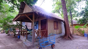 Una casa de madera rústica con techo de paja, un porche y un pequeño carruaje.