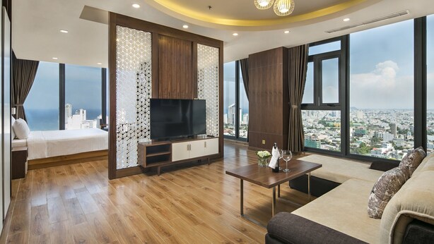 A modern living room with a large TV, wooden flooring, and a city view through large windows.