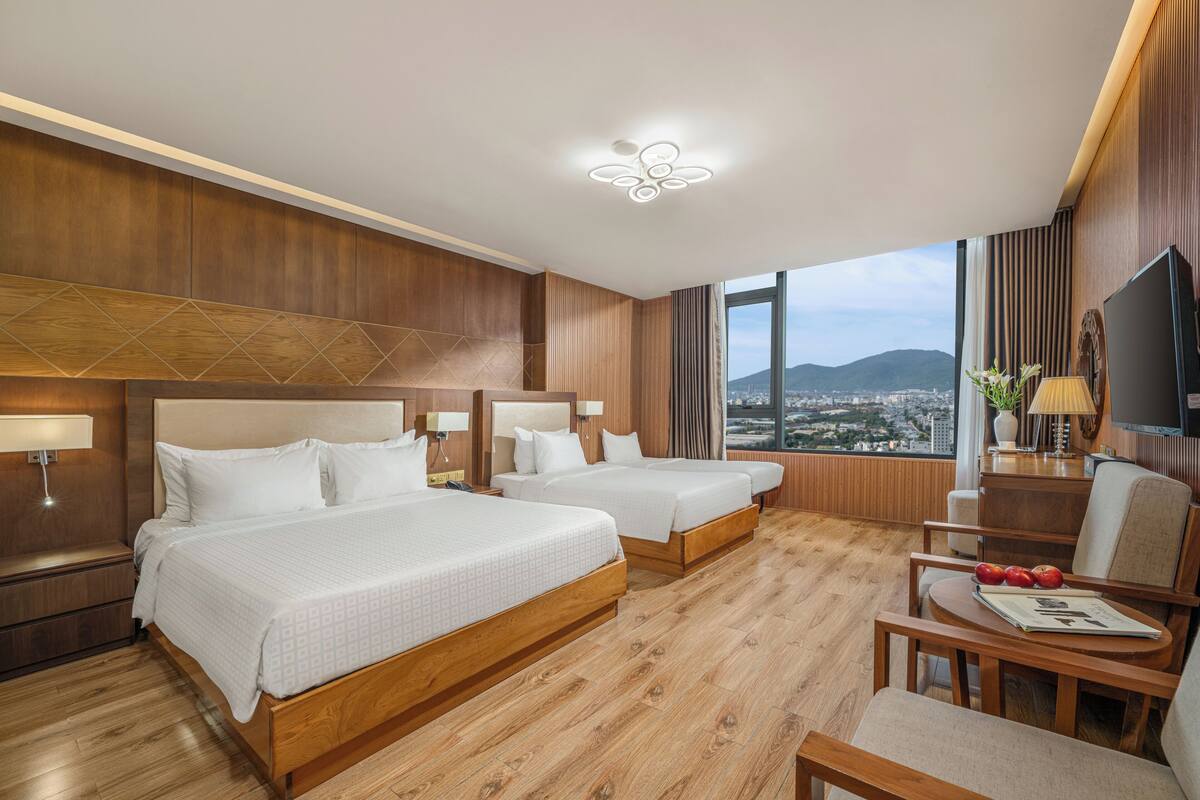 A hotel room with two beds, a TV, a desk with a chair, and a view of the city.