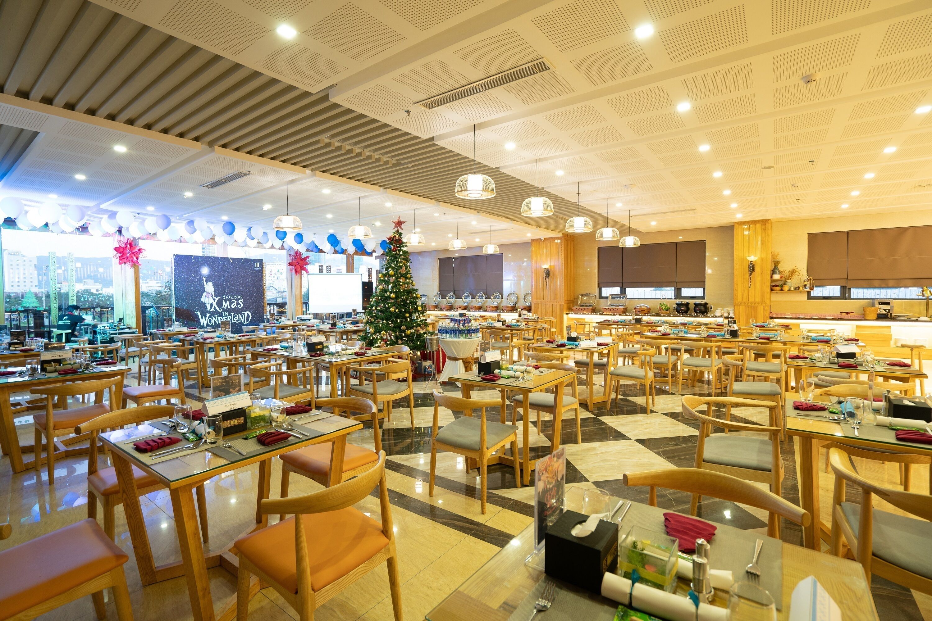 Un comedor amplio con varias mesas y sillas, un árbol de Navidad y un ventanal con vistas a la ciudad.