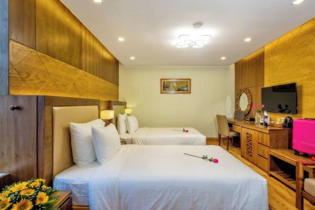 A hotel room with two beds, wooden paneling, a desk with a TV, and a painting on the wall.