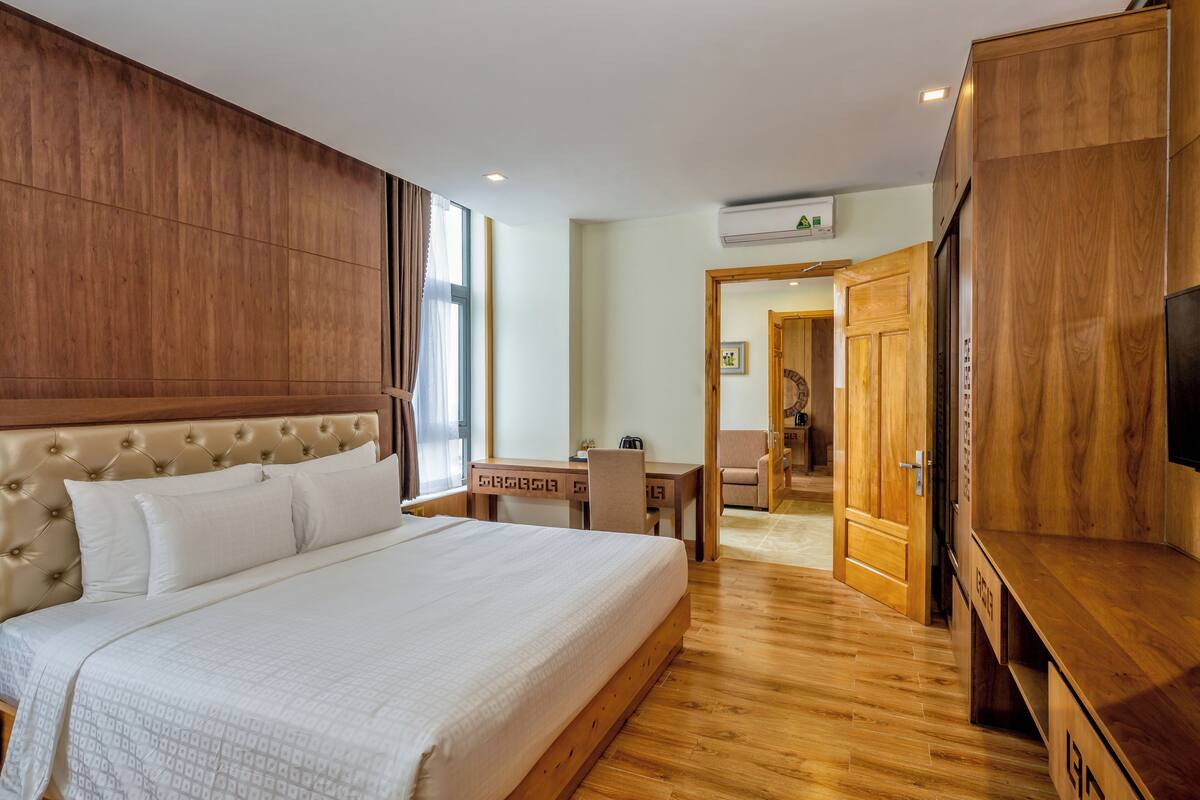 A hotel room with a large bed, wooden headboard, a desk, and a television.