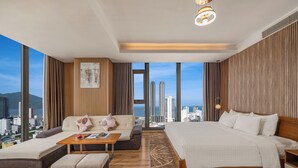 A modern hotel room with a large bed, a sofa, a coffee table, and a view of the cityscape.