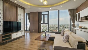 A modern living room with a flat-screen TV, wooden flooring, a sofa, a coffee table, and a city view through large windows.