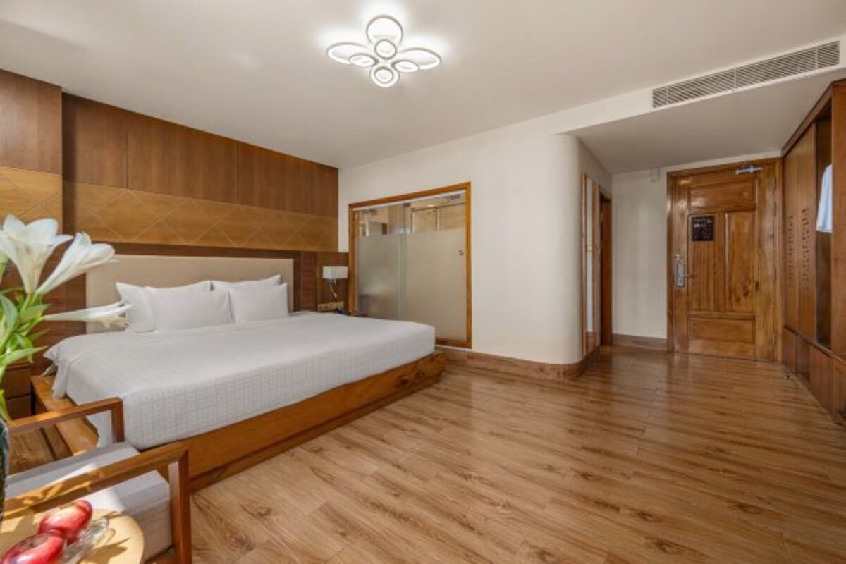 A bedroom with a wooden bed, a bedside table with a vase of flowers, and a wooden floor.