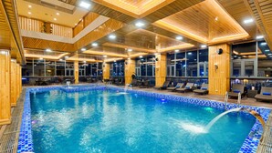A large indoor swimming pool with a blue-tiled edge, wooden paneling on the walls, and a modern ceiling design.