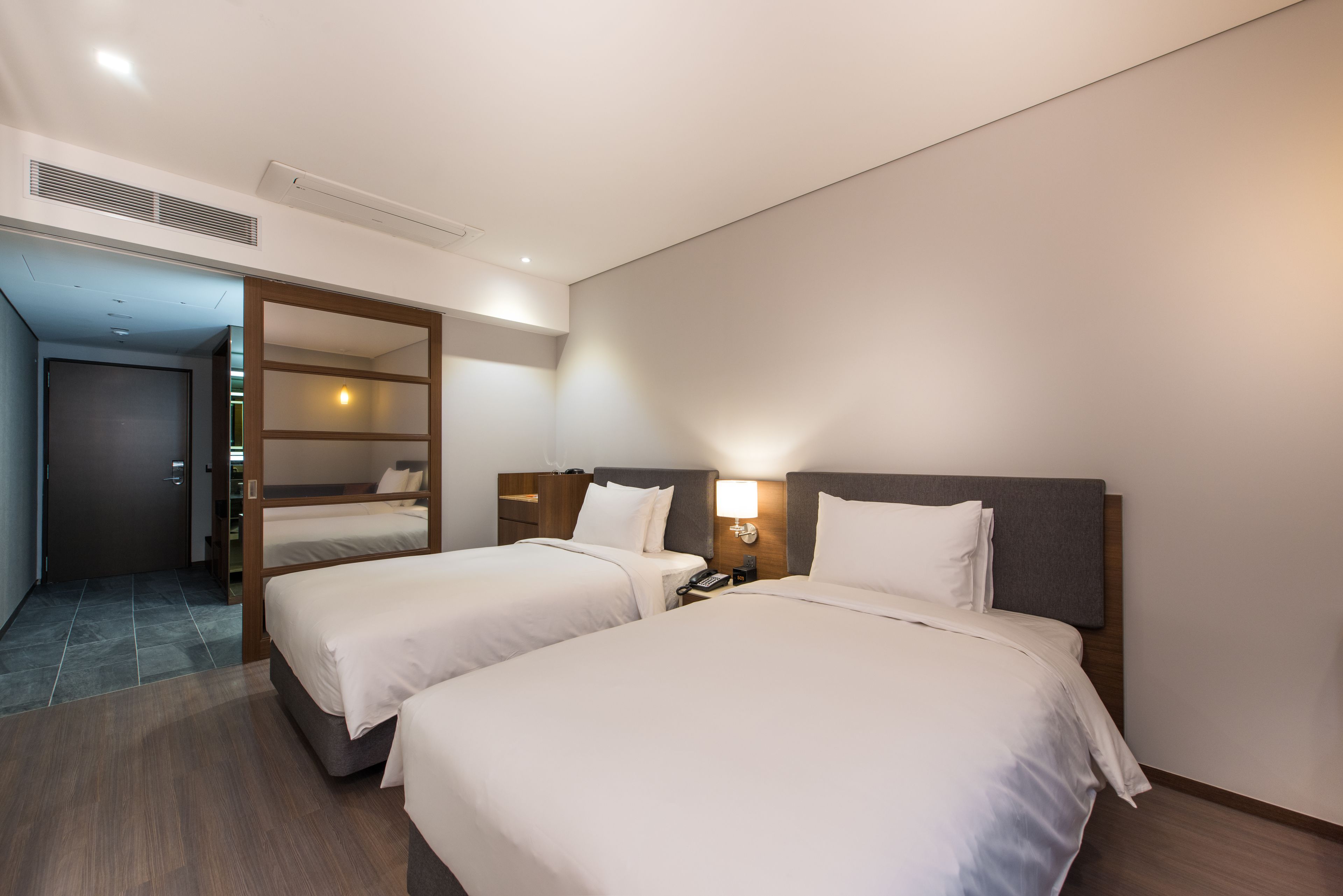 Una habitación de hotel con dos camas, un cabecero de madera, una lámpara de noche y un teléfono en la mesita.