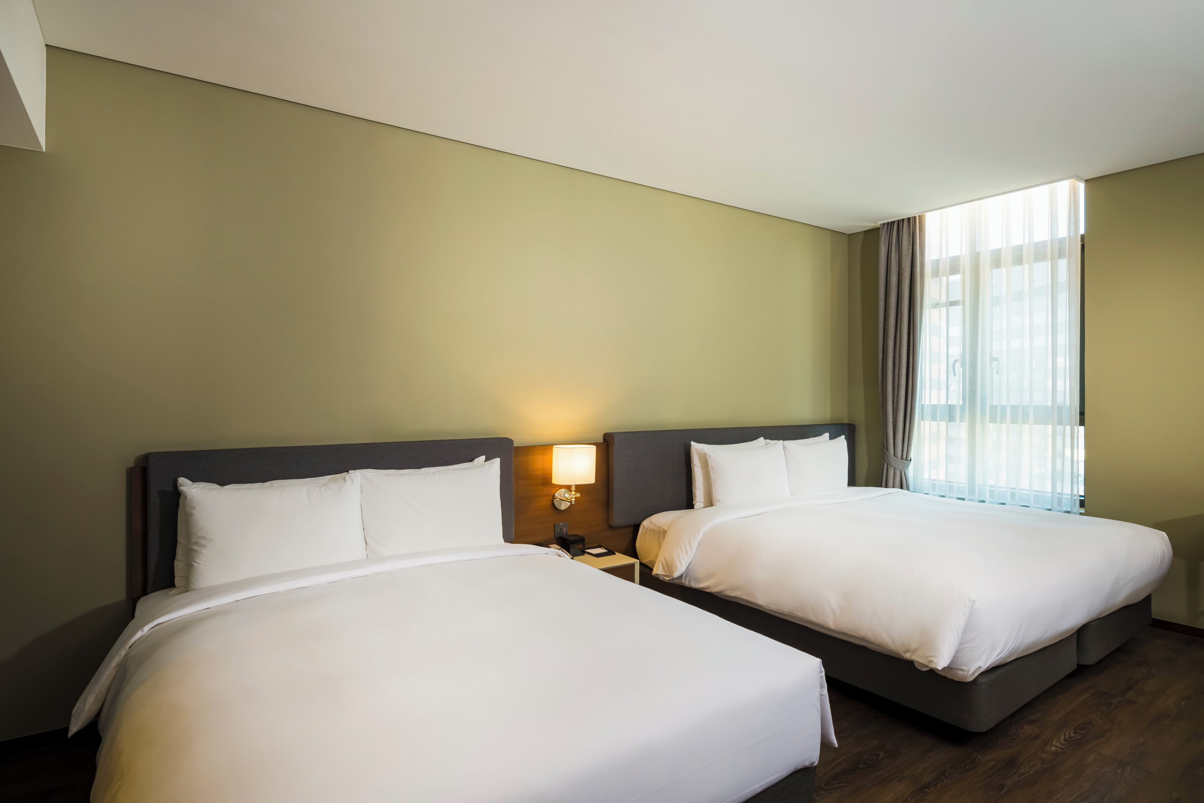 A hotel room with two beds, a nightstand with a lamp, and a window with curtains.