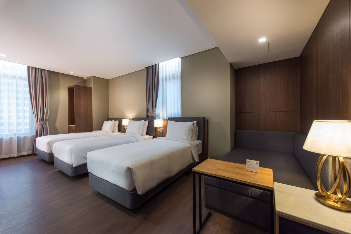 A hotel room with two beds, a sofa, a small table, and a lamp.
