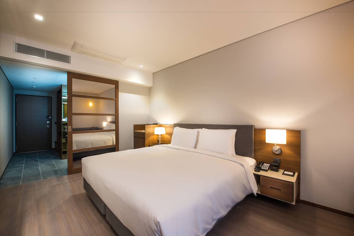 A hotel room with a large bed, two bedside tables with lamps, a wardrobe, and a door leading to a bathroom.