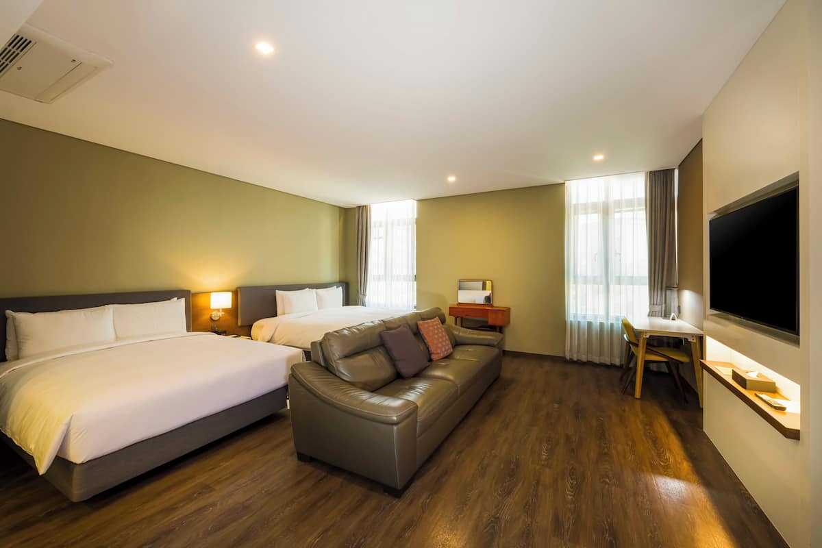 A hotel room with two beds, a sofa, a desk, and a TV.