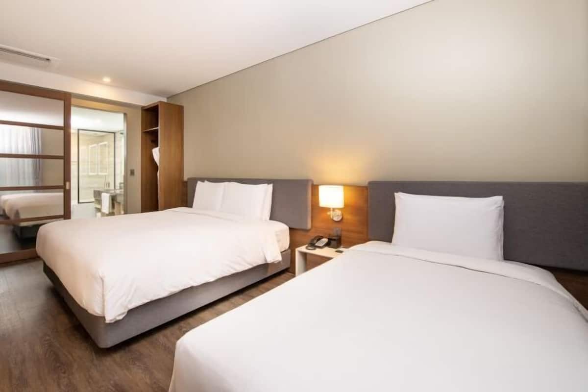 A hotel room with two beds, a bedside table with a lamp, and a mirror.