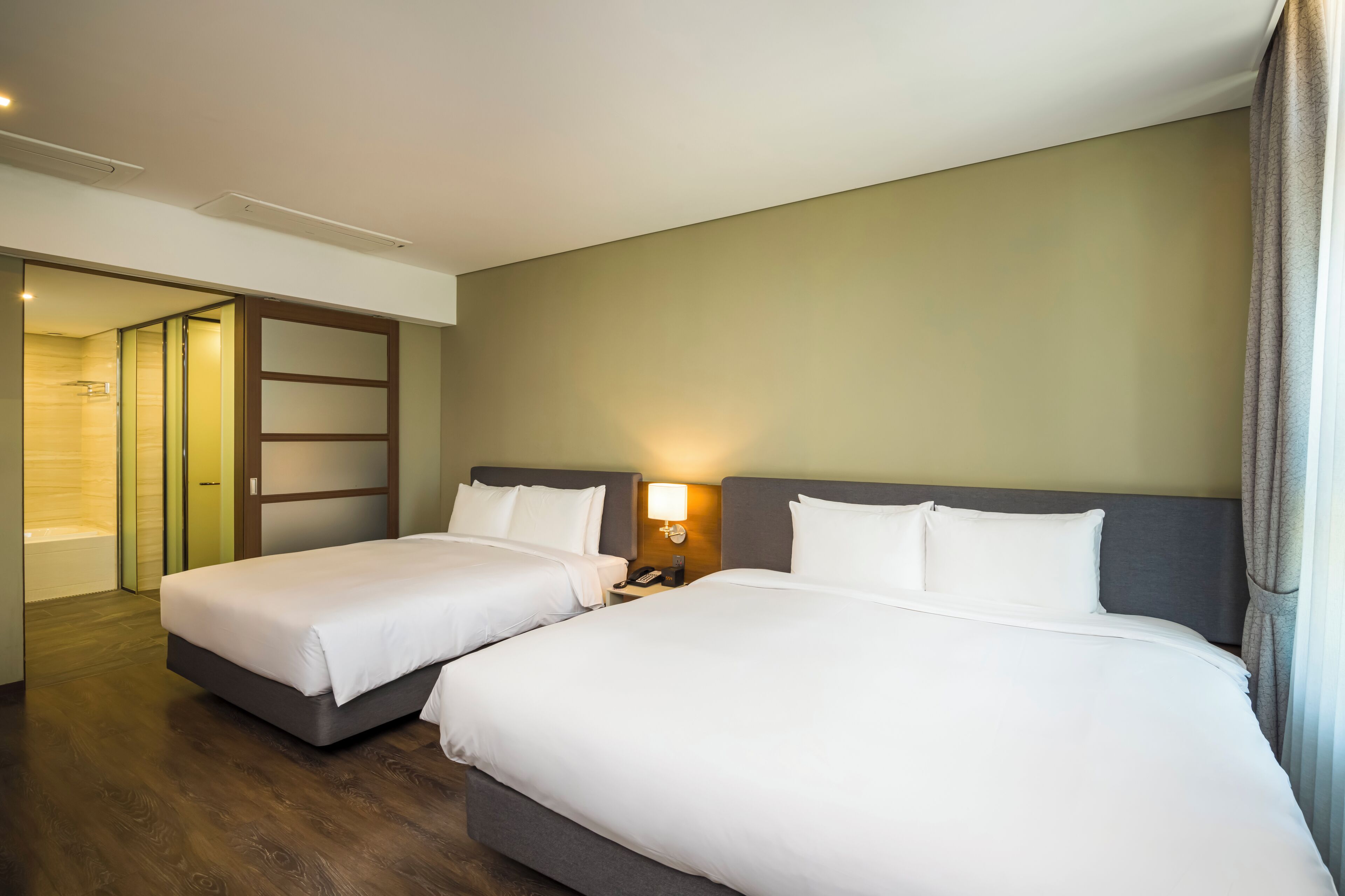Quarto de hotel com duas camas, um banheiro e uma mesa de cabeceira com abajur.